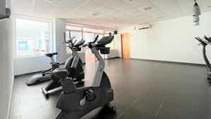 Un gimnasio con bicicletas estáticas y cintas de correr, amplias ventanas y piso de baldosas.