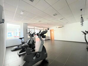 A gym with stationary bikes and treadmills, large windows, and a tiled floor. - Belvilla by OYO Vereda Golf II (Roquetas de Mar)