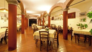 Un vaste espace dédié à la salle à manger, avec de nombreuses tables et chaises, des arches en briques et un sol carrelé.