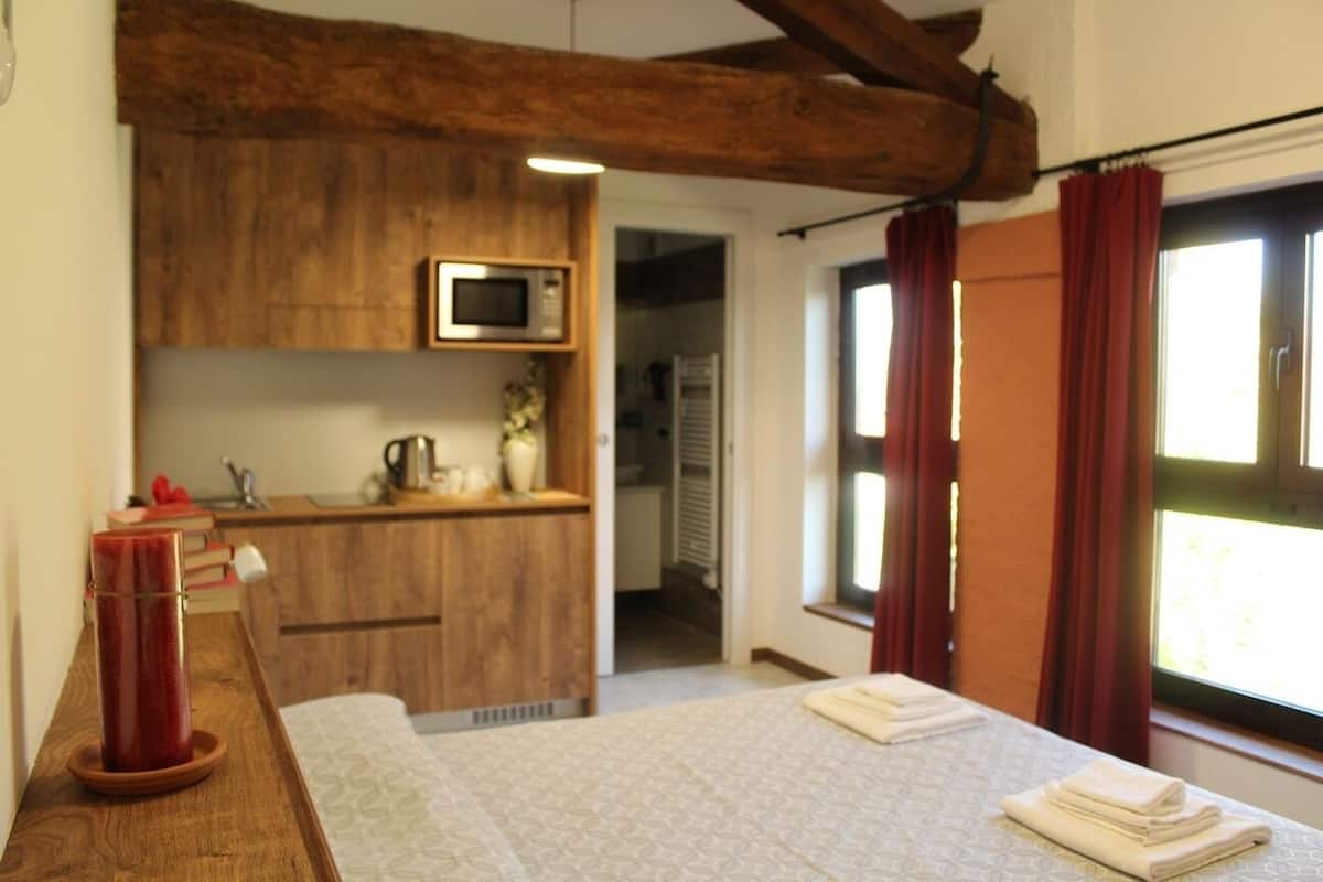 Une chambre avec un lit, un bureau en bois doté d’un micro-ondes et une fenêtre avec des rideaux.