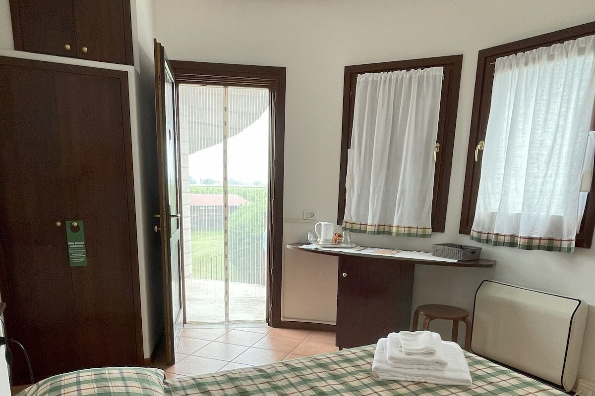 Une chambre d’hôtel avec un lit, un bureau et une chaise. Une porte donne accès à un espace extérieur.