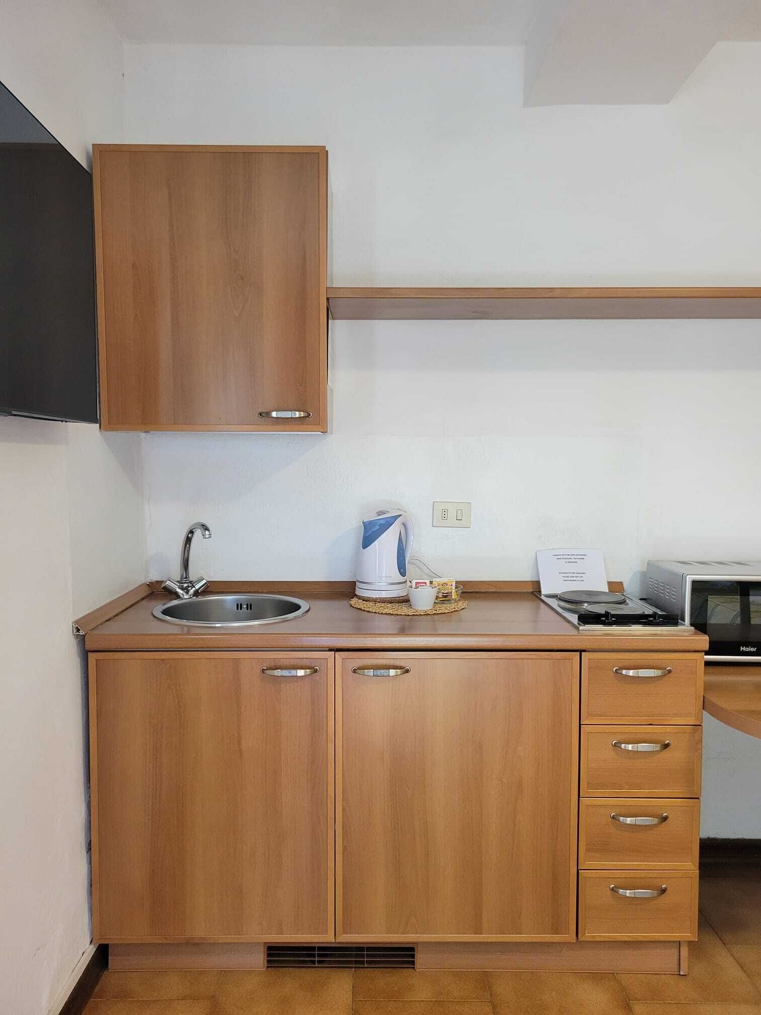 A kitchen with wooden cabinets, a sink, a kettle, a microwave, and a toaster.