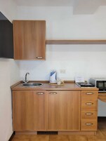 Una cocina con armarios de madera, un lavamanos, una tetera, un microondas y un tostador.