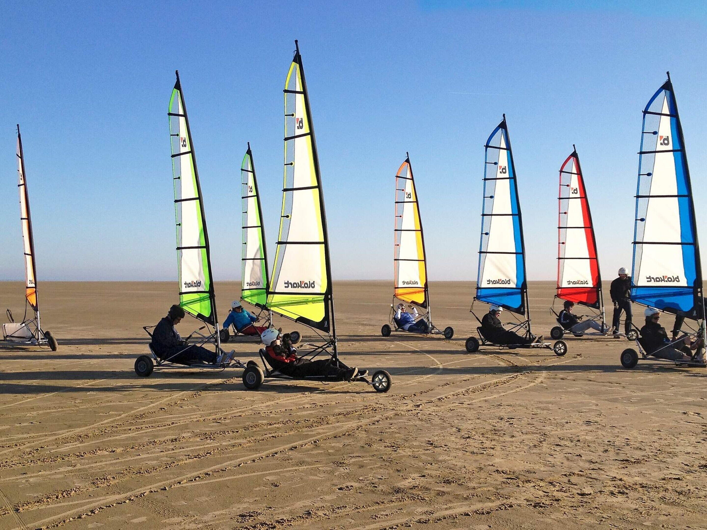 A beach with multiple windsurfing carts and colorful sails.