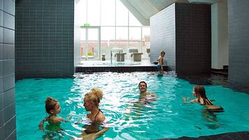 En indendørs swimmingpool med flisebeklædte vægge og et skråt tag.
