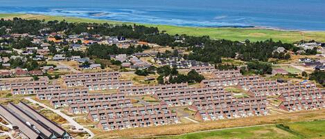 A coastal residential area with multiple rows of houses, a golf course, and a large body of water in the background.