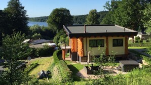 A modern house with a sloped roof, surrounded by lush greenery and a lake view. - Canadian Log Cabin Comfortable Holiday Residence (Stuer)