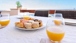 Een ontbijttafel met croissants, muffins en sapglazen, met uitzicht op de oceaan.