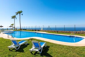 A swimming pool with two lounge chairs, a stone wall, and a view of the ocean. - Apartment in Spain Near the Beach (Rincon de la Victoria)