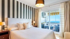 Een hotelkamer met een groot bed, uitzicht op zee en een balkon met zitplaatsen buiten.