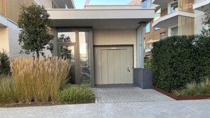 A modern building entrance with a paved driveway, a glass door, and a wooden fence. - Apartment in Nieuwpoort Near the Marina (Nieuwpoort)