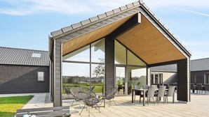 A modern outdoor patio with a wooden pergola, seating area, and a fire pit. - 5 Star Holiday Home in Norre Nebel (Norre Nebel)