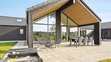A modern outdoor patio with a wooden pergola, seating area, and a fire pit.