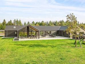 A modern building with a large patio area, a covered seating area, and a view of a forested area. - 5 Star Holiday Home in Norre Nebel (Norre Nebel)