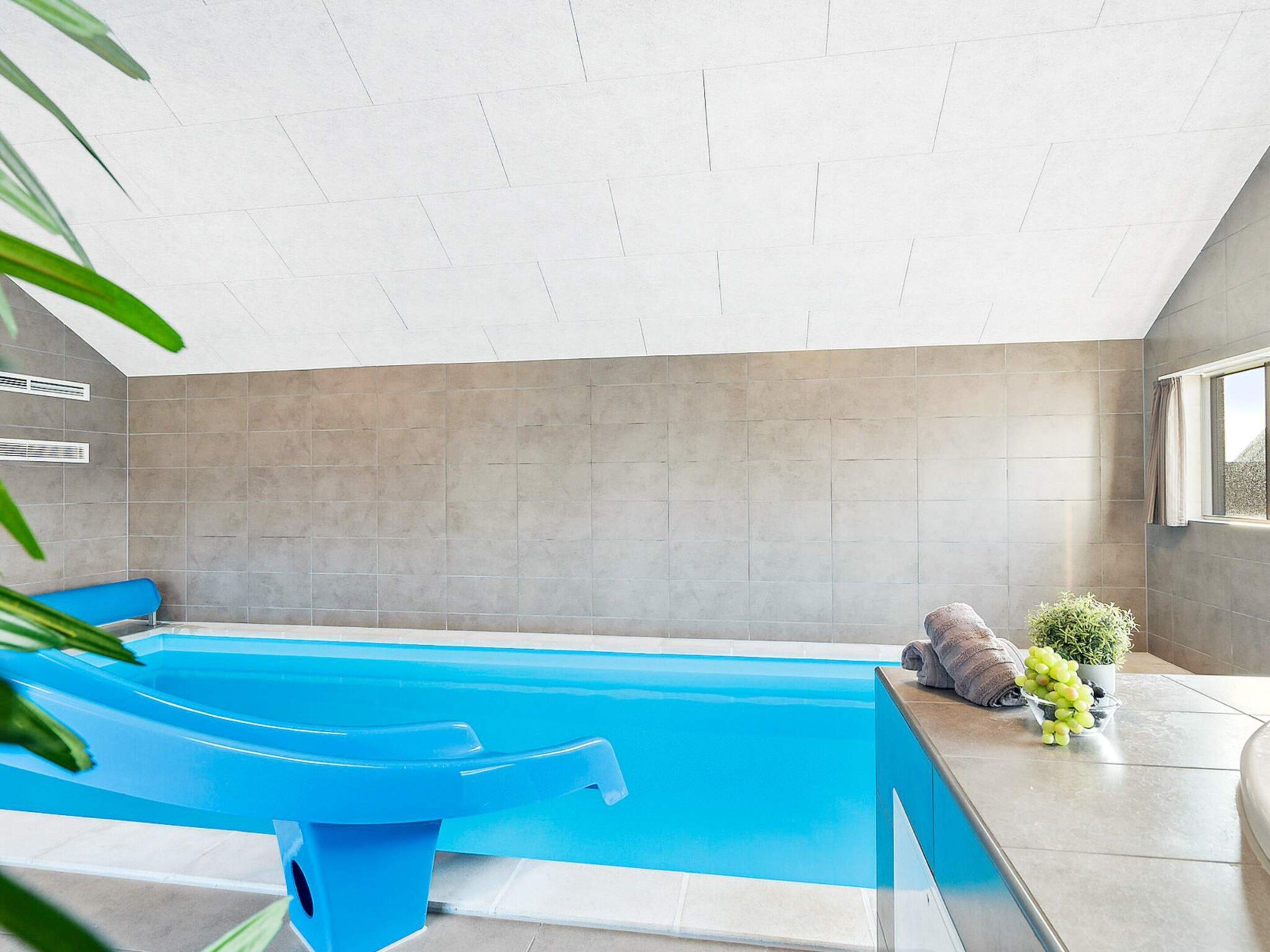 Una piscina interior moderna con un tobogán azul, una toalla y una planta en maceta.
