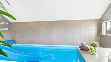 Una piscina interior moderna con un tobogán azul, una toalla y una planta en maceta.