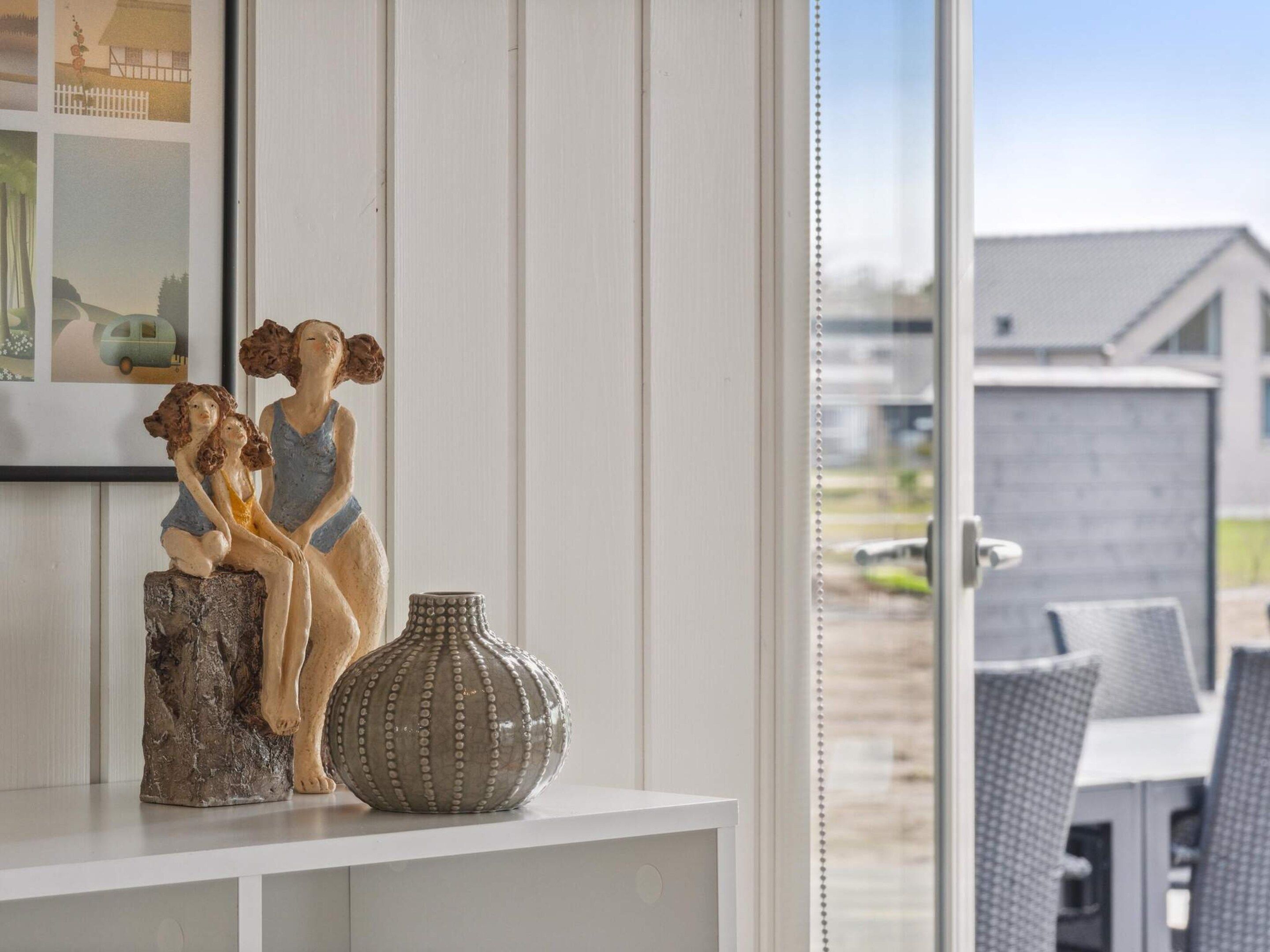 Una habitación con un estante blanco que sostiene una escultura de dos figuras y un jarrón decorativo.