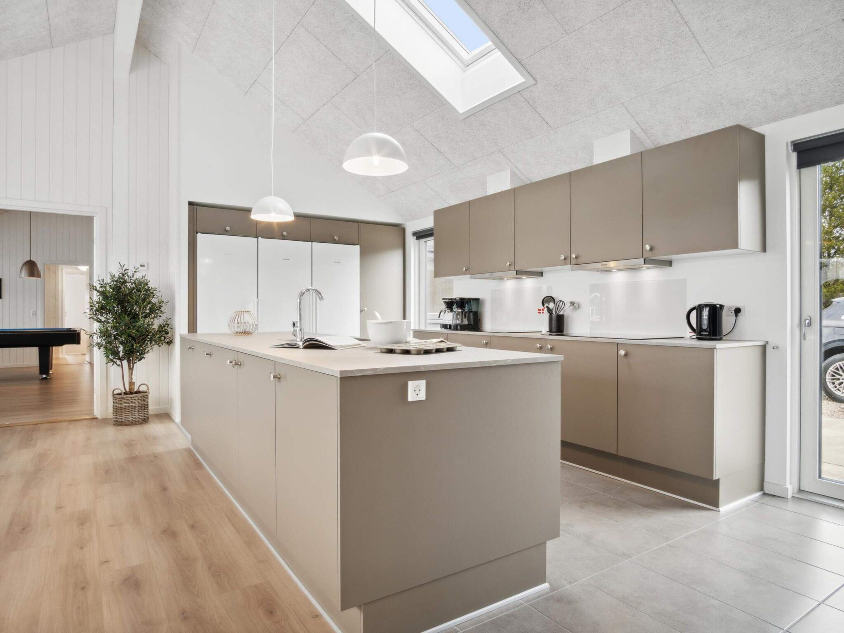 A modern kitchen with a central island, pendant lighting, and a view of the outdoors through a skylight.