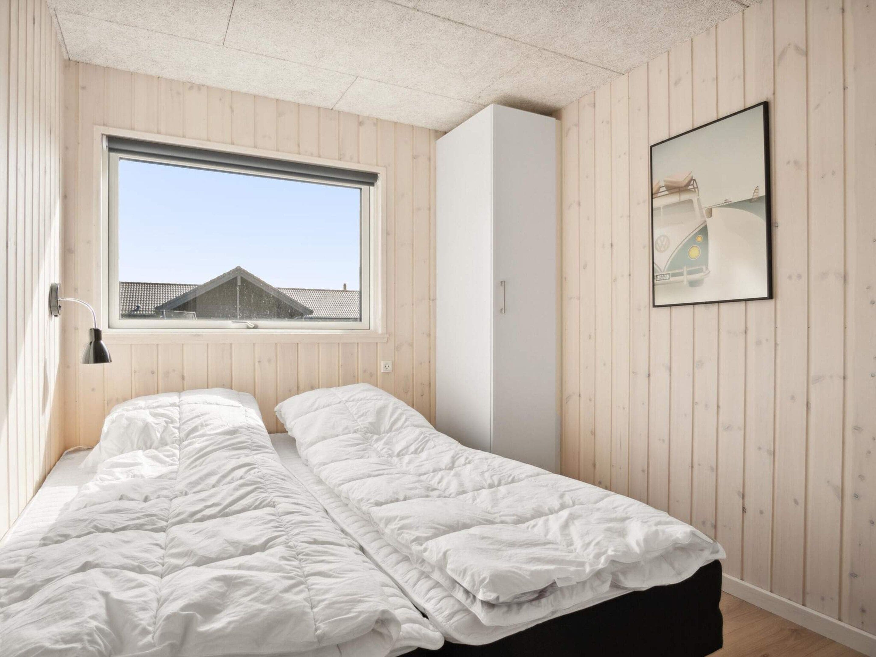 A bedroom with a bed, a window, a wardrobe, and a framed picture on the wall.