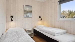 A room with two beds, a nightstand, a wall-mounted picture, and a window with a view of trees. - 5 Star Holiday Home in Norre Nebel (Norre Nebel)