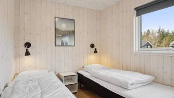 A room with two beds, a nightstand, a wall-mounted picture, and a window with a view of trees.