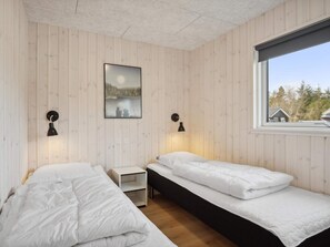 A room with two beds, a nightstand, a wall-mounted picture, and a window with a view of trees. - 5 Star Holiday Home in Norre Nebel (Norre Nebel)