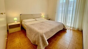 Une chambre à coucher comprenant un lit, deux tables de chevet, une commode, une fenêtre avec des rideaux et un plancher en bois.