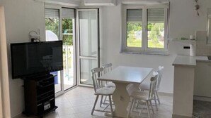 Uma cozinha moderna com uma mesa de jantar e cadeiras, uma televisão e uma porta de vidro deslizante para uma varanda.