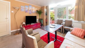 Un moderno salón con televisor de pantalla plana, mueble de entretenimiento rojo, sofás beige, alfombra roja y un ventanal con vistas a la vegetación.