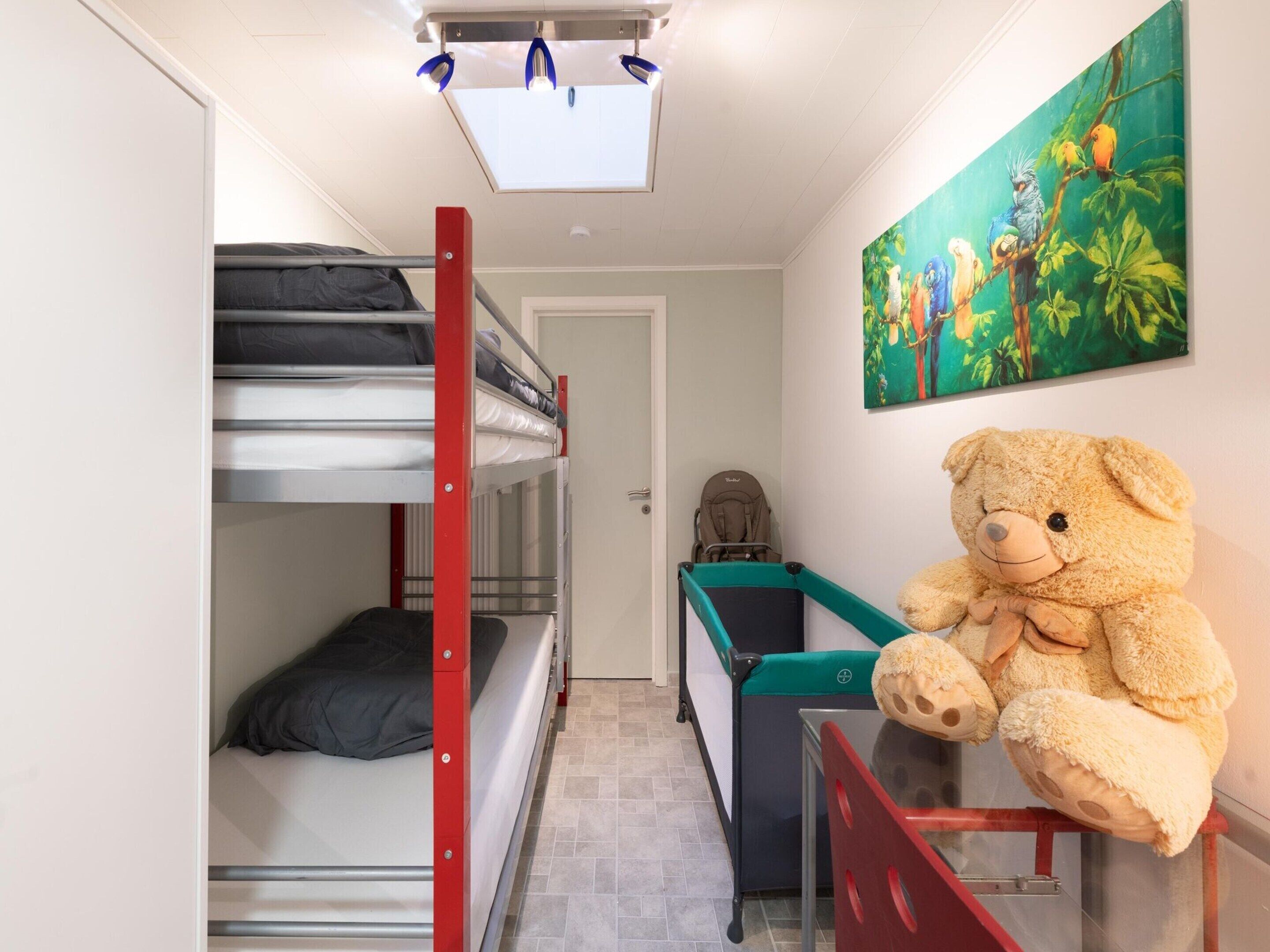 Habitación tipo dormitorio con literas, una cuna, un oso de peluche y un cuadro de pájaros.