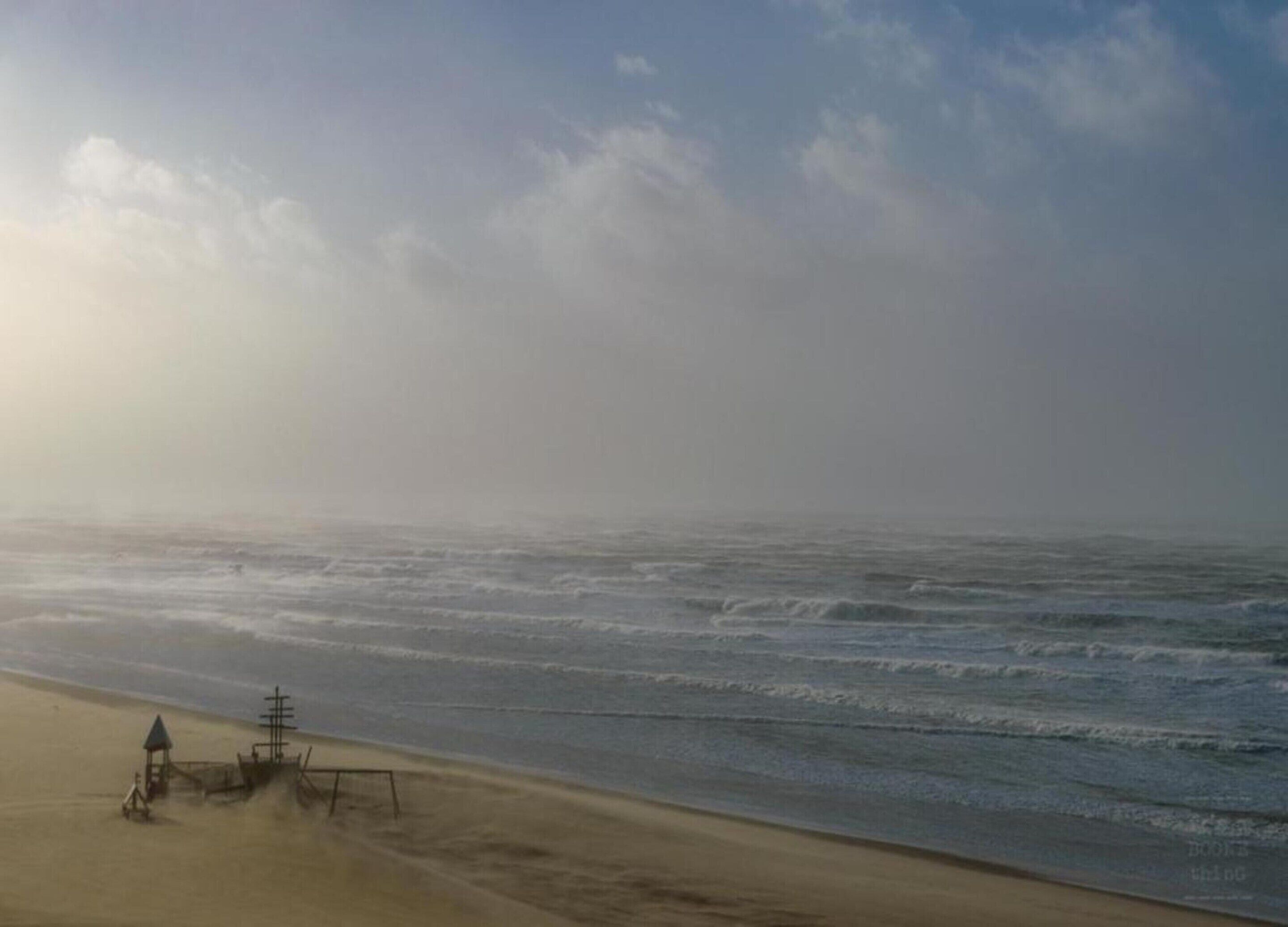Ein Strand mit einem Rettungsturm und einer kleinen Struktur, vermutlich eine Rettungswache, im Sand.