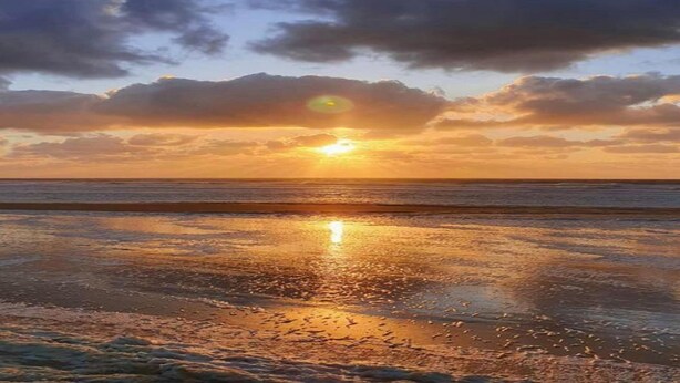 Un atardecer sobre una playa con aguas tranquilas que reflejan el cielo.