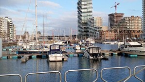 Puerto deportivo con barcos amarrados, un edificio moderno en construcción y un cielo despejado.