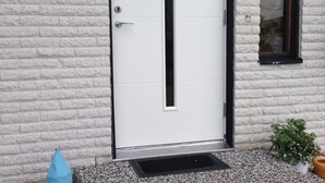 A white door with a black frame, a small window with a dark frame, and a potted plant to the right. - 4 Star Holiday Home in Bonassund-by Traum (Bonässund)