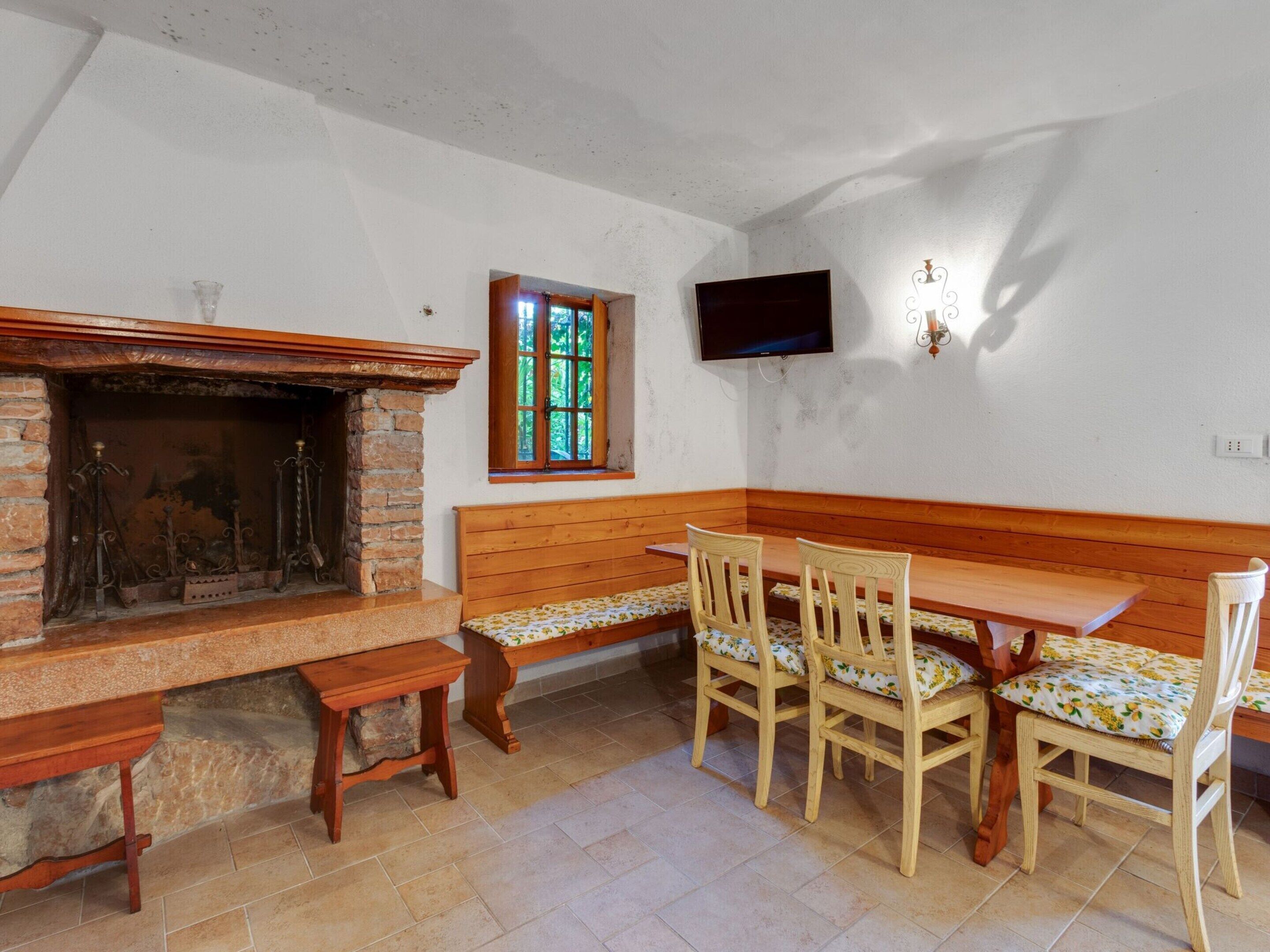 Un coin repas avec un banc et des chaises en bois, une cheminée en pierre et un téléviseur fixé au mur.