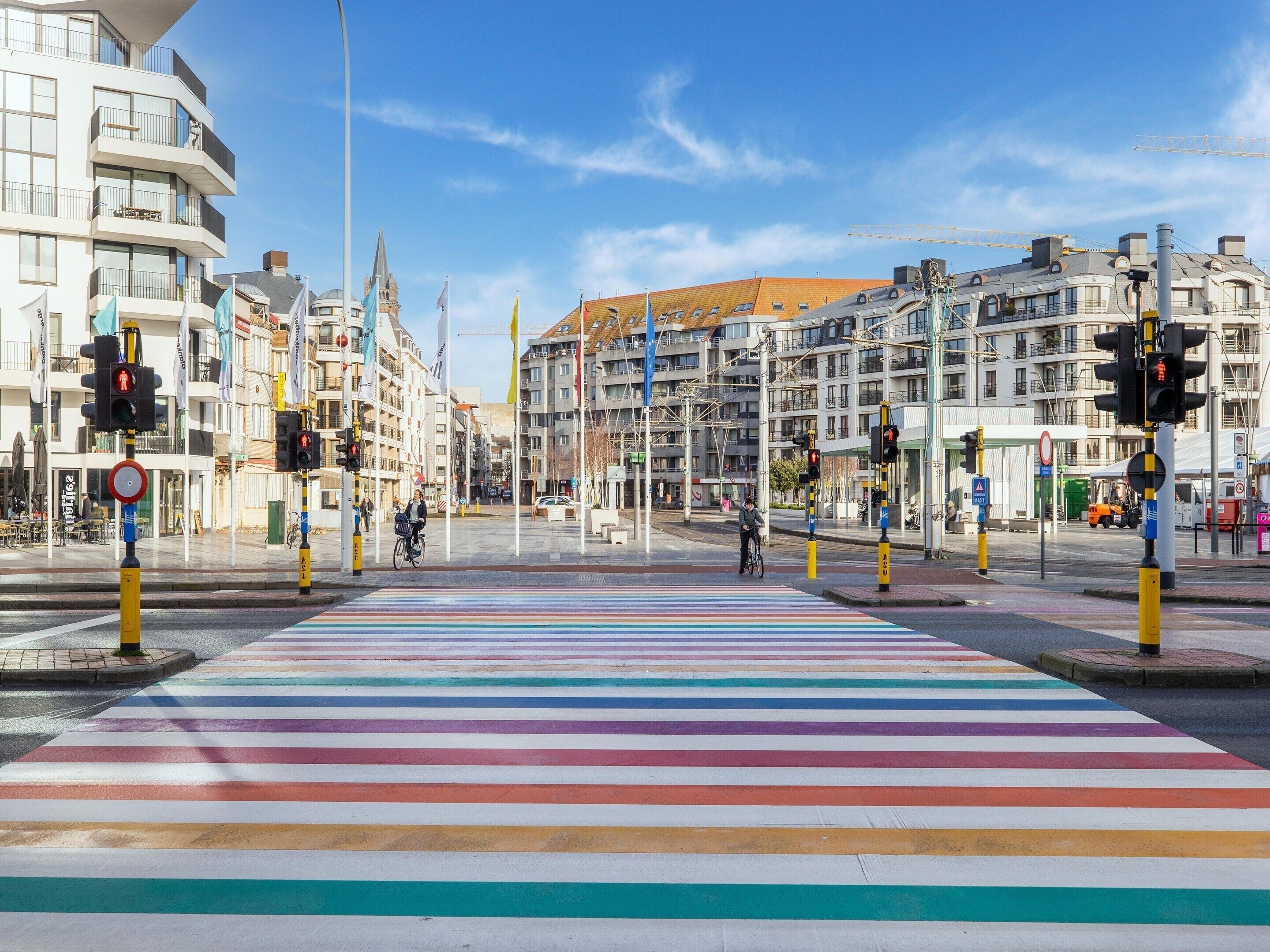 A pedestrian crossing with colorful stripes, traffic lights, and buildings in the background.