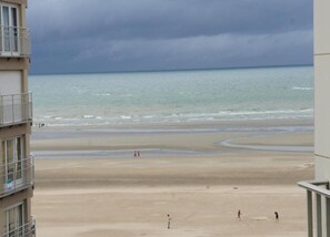 A beach view from a building with balconies overlooking a sandy beach and the sea under a cloudy sky. - Apartment in Koksijde Near the Beach (Koksijde)