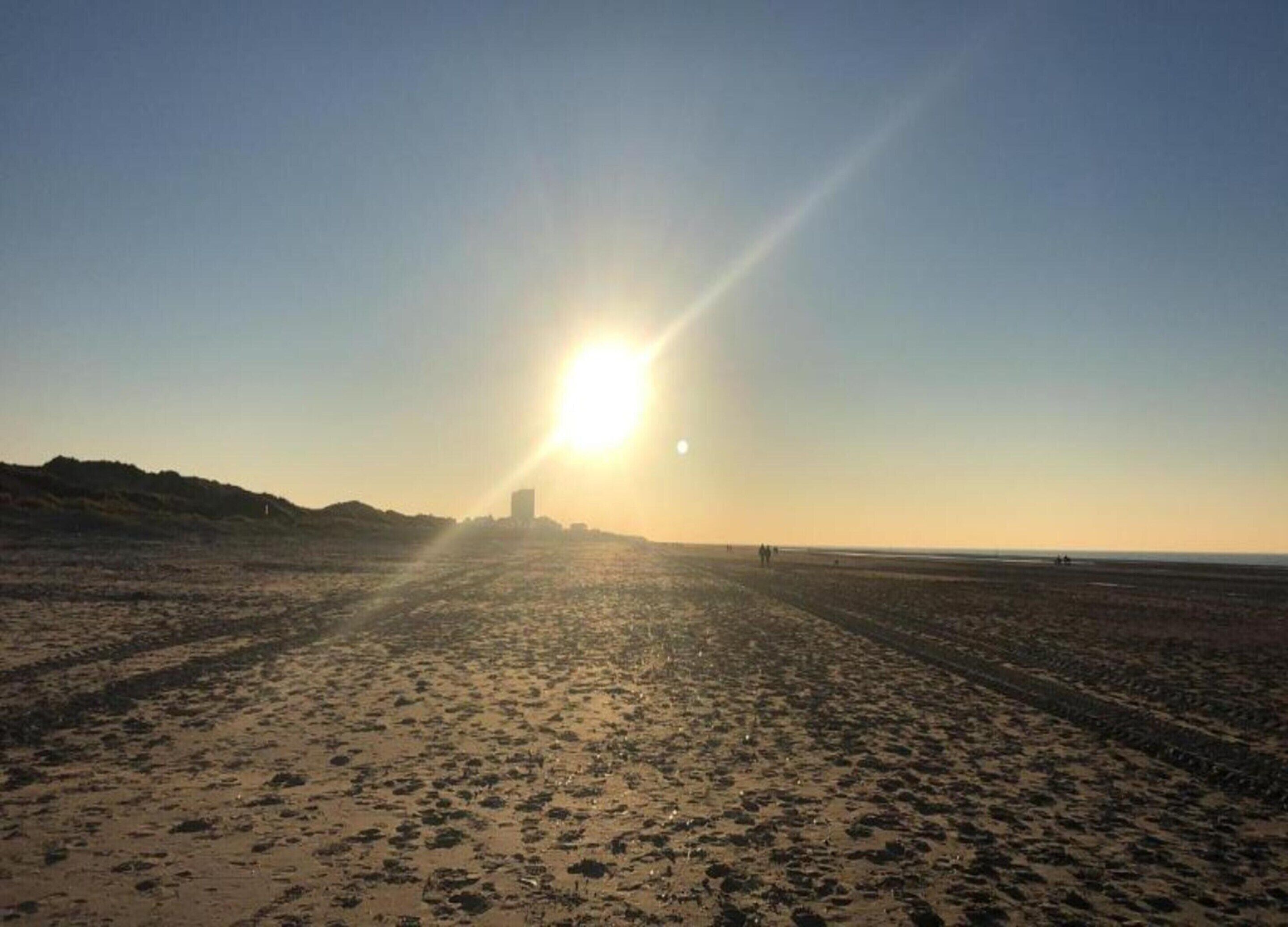 Ein Strand mit tiefstehender Sonne am Horizont, der lange Schatten wirft.