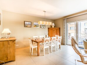 Un comedor con una mesa de madera y sillas blancas, un armario de madera, y una ventana con vistas a edificios.
