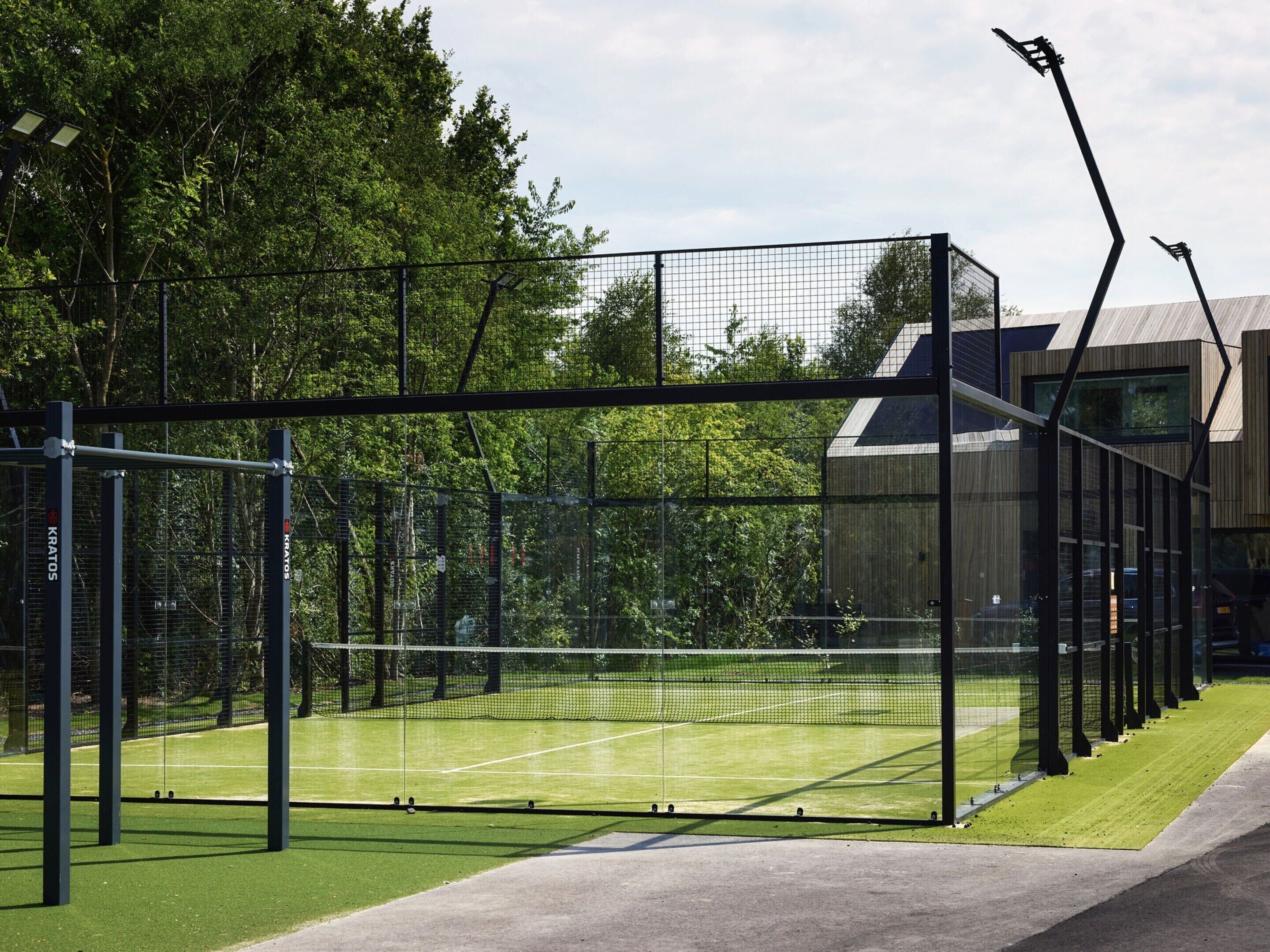 Ein Tennisplatz mit Netz, umzäunt und mit Bäumen im Hintergrund.