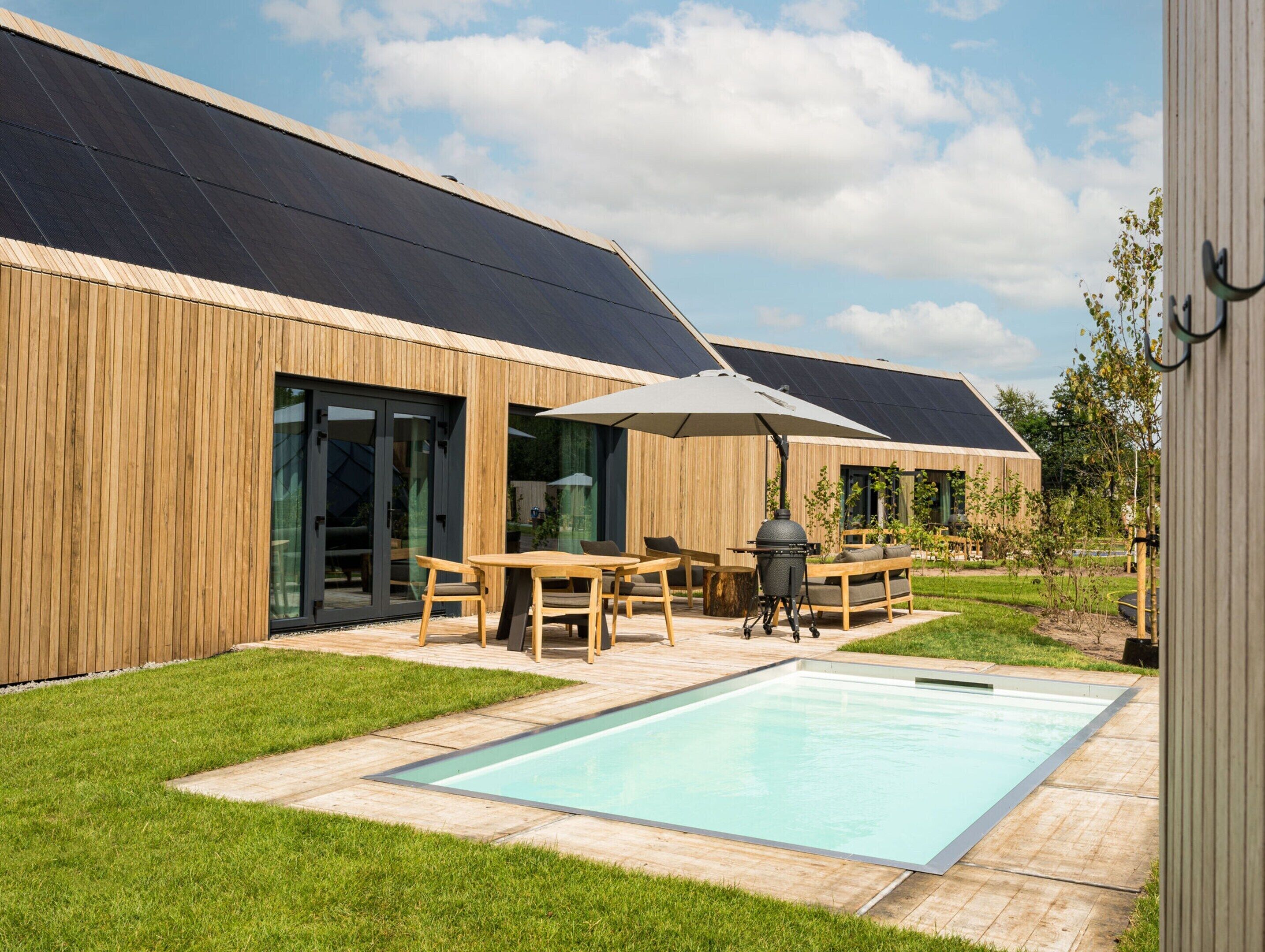 A modern house with a pool, wooden exterior, and solar panels.