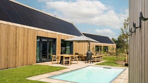 A modern building with a wooden exterior, a swimming pool, and outdoor seating. - Holiday Home in Drenthe With Private Pool (Appelscha)