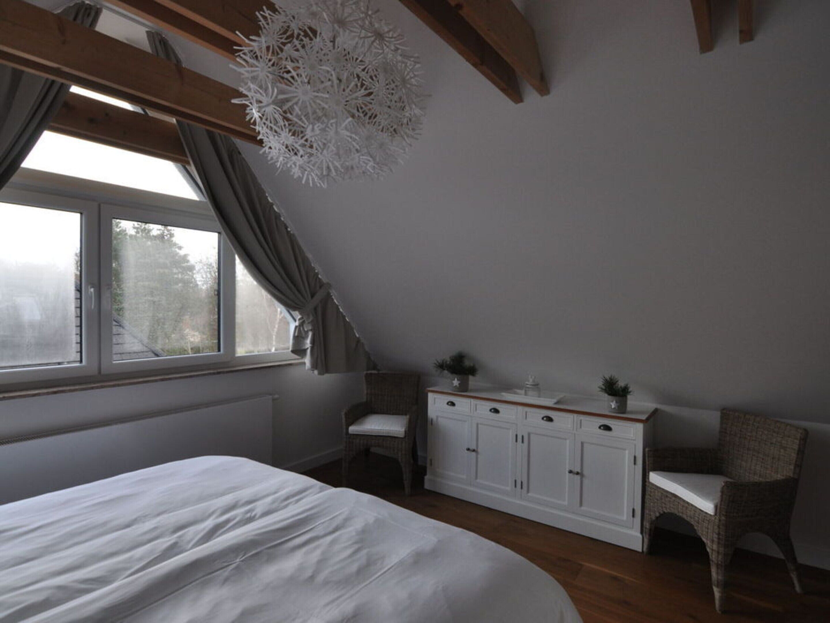 Un dormitorio con una cama grande, un aparador blanco, una silla y una ventana con cortinas.