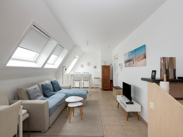 Un apartamento moderno y luminoso con techo tipo loft, un sofá, una mesita, un televisor y una zona de cocina.
