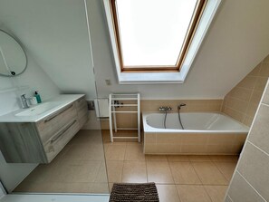 Un baño moderno con tragaluz, bañera, tocador con espejo y zona de ducha.