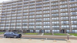 A multi-story residential building with a uniform facade, balconies, and a parking area with a car. - Cozy and Spacious Apartment on the 1st Floor (Middelkerke)