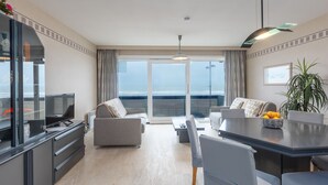 A modern hotel room with a balcony, a dining area, and a TV. - Cozy and Spacious Apartment on the 1st Floor (Middelkerke)