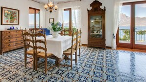 Ein Essbereich mit Tisch, Stühlen und einer Chandelier. Es gibt eine Vitrine mit Glastüren und Blick auf das Meer durch einen Balkon.