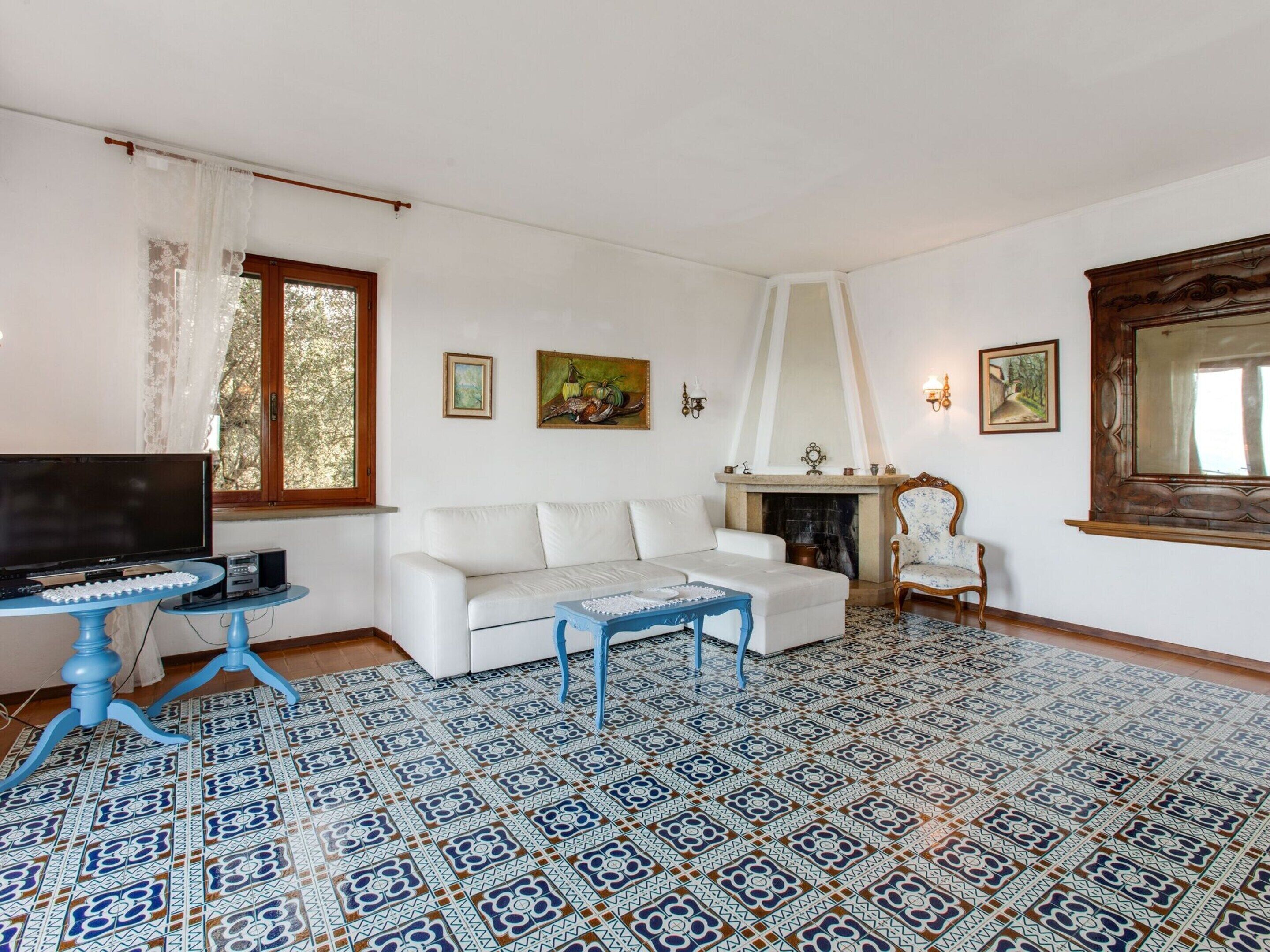 A living room with a white sofa, a blue coffee table, a television on a stand, a fireplace, and patterned floor tiles.