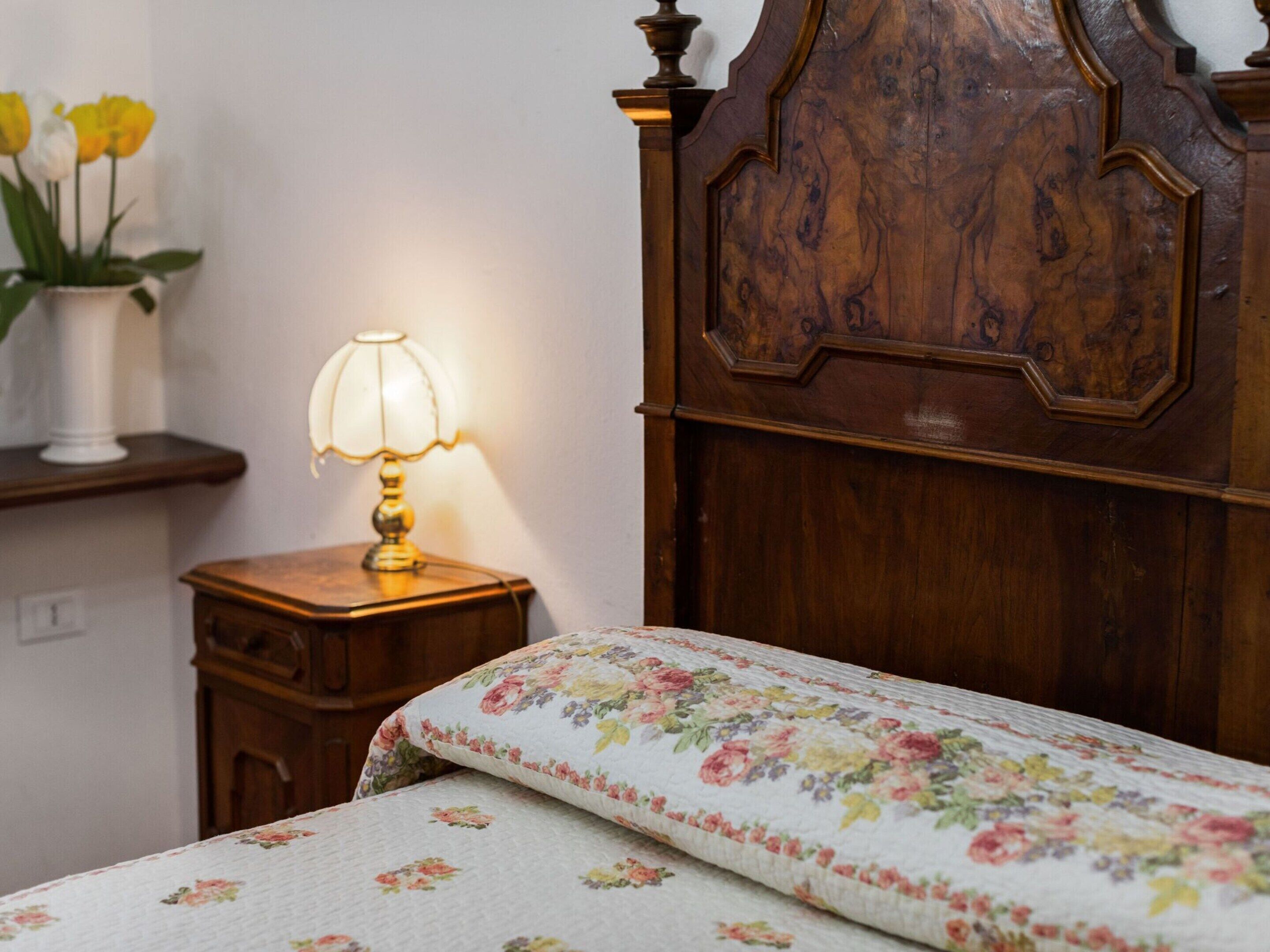 A bedroom with a wooden headboard, a bedside table with a lamp, and a floral bedspread.